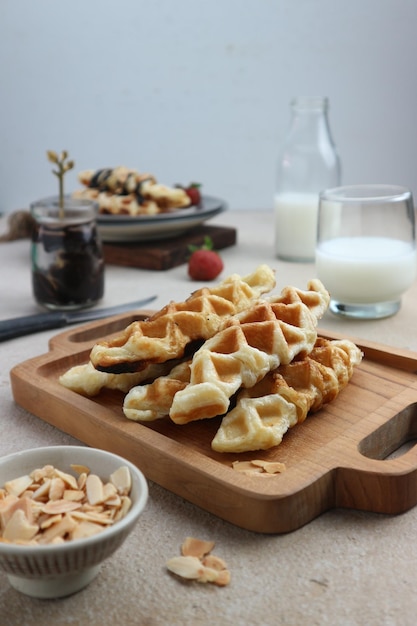 A wooden cutting board with waffles and a plate of almonds on it.