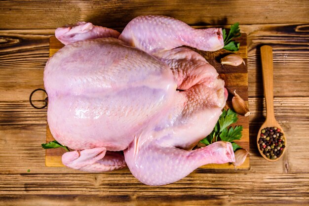 Wooden cutting board with the whole uncooked chicken garlic and spices Top view