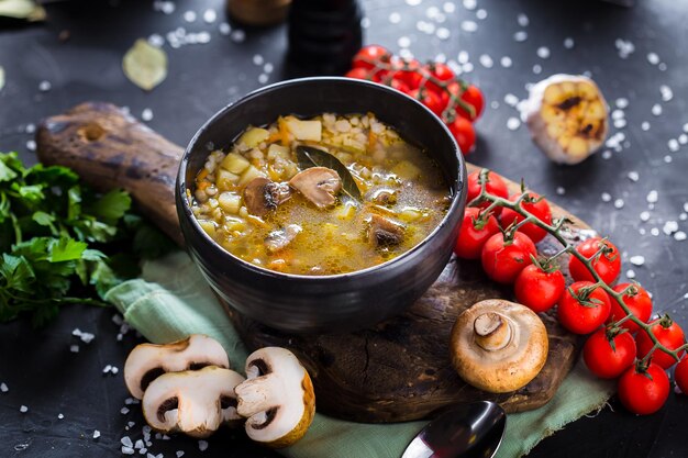 на деревянной разделочной кухонной доске, суп с грибами и ячневой кашей, помидоры черри, столовые приборы
