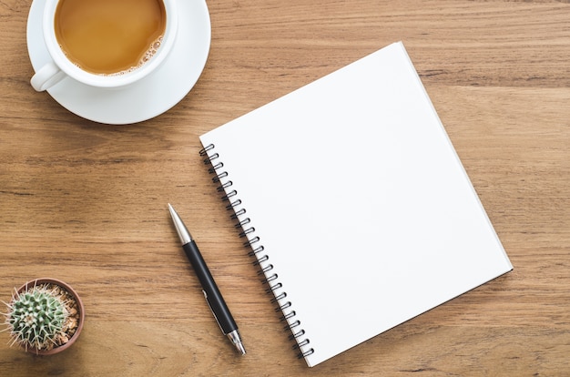 Wooden desk table with notebook, pen, cactus and cup of coffee. Top view with copy space.