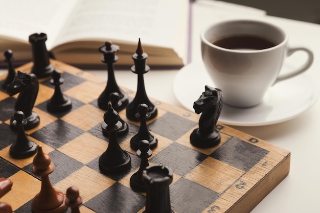 Wooden desk with chess play, book and cup of coffee on white table. Board game, intelligence and brain upgrade concept