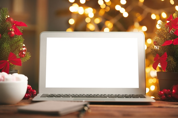 Wooden desk with computer with blank screen against blurred christmas lights background