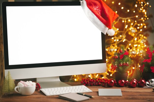 ぼやけたクリスマスライトの背景に対して空白の画面を持つコンピューターと木製の机