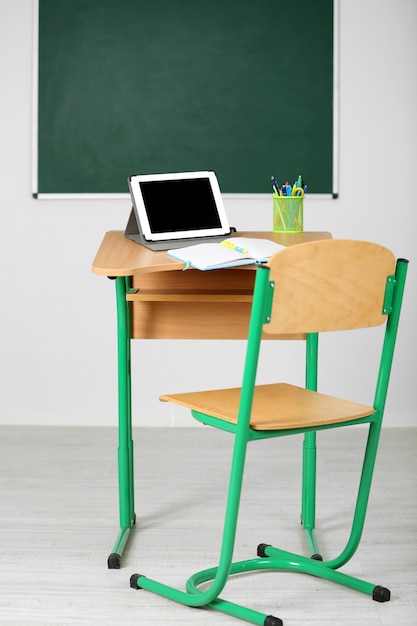 Фото Деревянный стол с канцелярскими принадлежностями и планшетом в классе на фоне доски