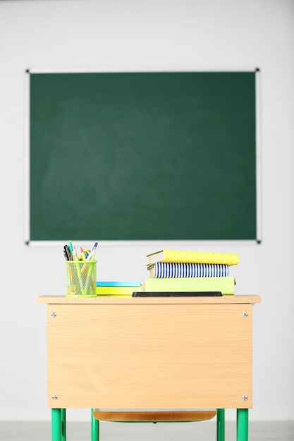 wooden desk with stationery and chair in class on blackboard background