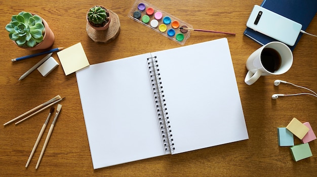 wooden desktop with watercolor painting tools, an open notebook, and brushes