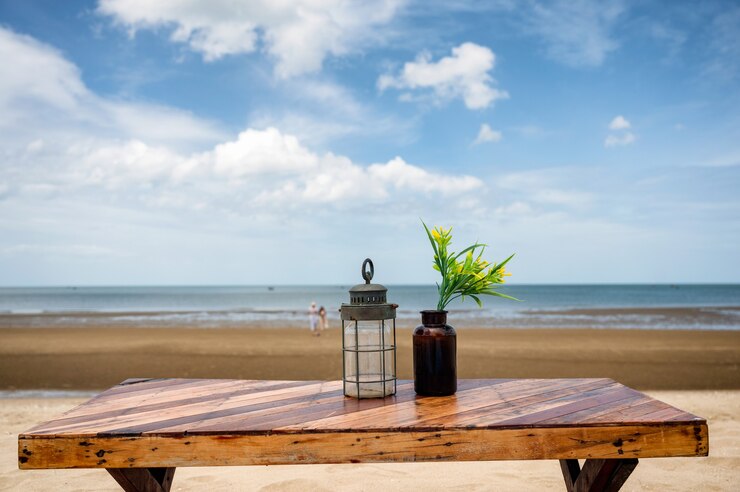 Photo wooden dining table with lantern and flower in glass on the beach and blue sky on summertime