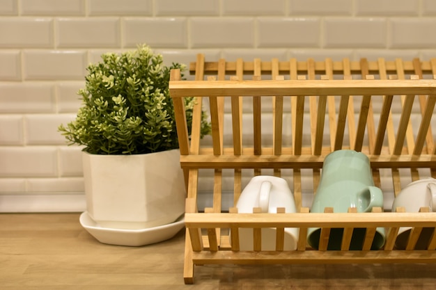 Wooden dish rack and tea cups in modern kitchen interior against background of brick wall
