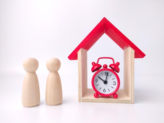 Wooden doll figures of couplealarm clock and toy house on a\
white background