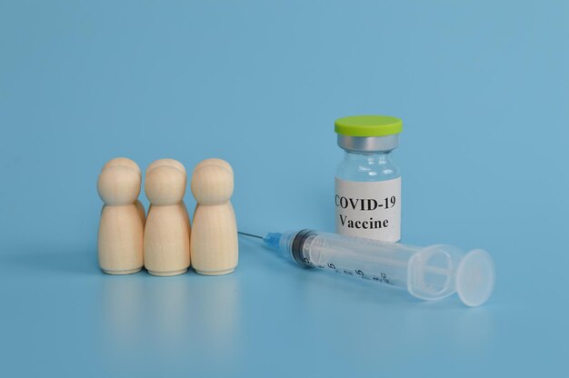 Wooden doll figures of people syringe and covid19 vaccine on\
blue background