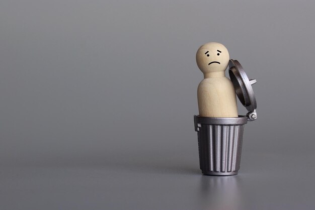Wooden doll inside trash can down in the dumps depressed sad\
and miserable concept copy space