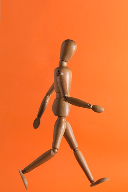 Wooden doll walking on an orange background