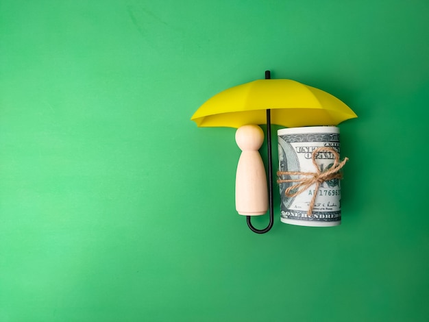 Photo wooden dolls and banknotes are hiding under a yellow umbrella with copy space