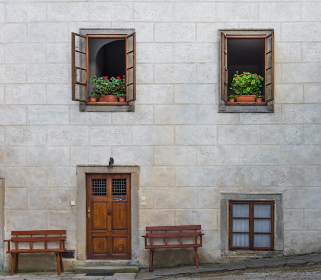 Wooden door on empty concrete gray blocks wall with upper two windows opening decorated with flower