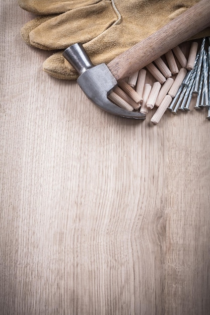 Wooden dowels claw hammer leather working gloves and stainless nails on wood board copy space construction concept