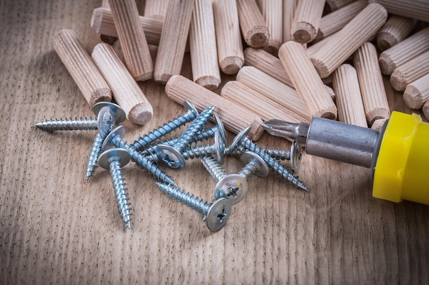 Wooden dowels construction nails and insulated screwdriver on wood board