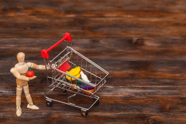 Wooden dummy puppet with mini shopping cart. Abstract food concept