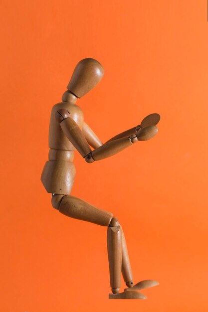 Photo wooden dummy that takes a sitting position in the air like driving located on an orange background