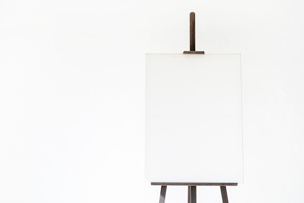 Wooden easel with blank canvas on light background for mockup\
design