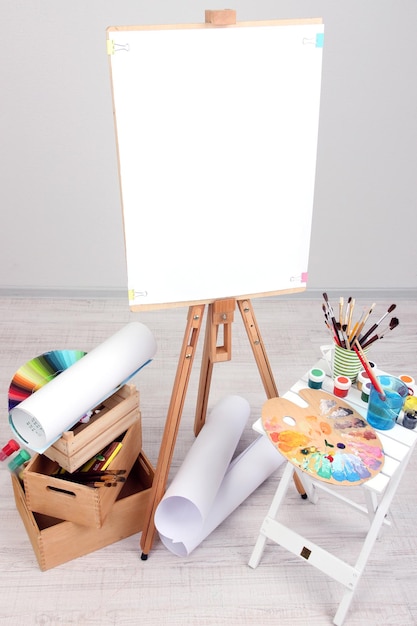 Photo wooden easel with clean paper and art supplies in room