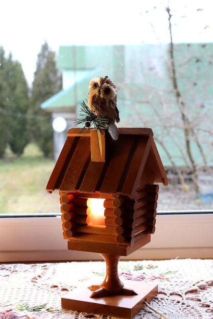A wooden electric retro lamp in the form of a hut on chicken legs with a toy owl on a chimney a fairytale house with a burning window Vertical photo closeup