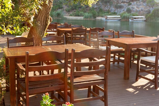 Wooden empty tables with massive chairs in restaurant on river bank Horizontal photo