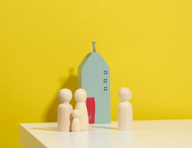 Деревянные семейные фигурки, модельный дом на желтом фоне. покупка недвижимости, концепция аренды. переезд в новые квартиры