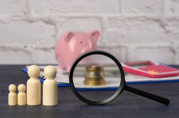 Wooden family figurines and  pink ceramic piggy bank on blue surface