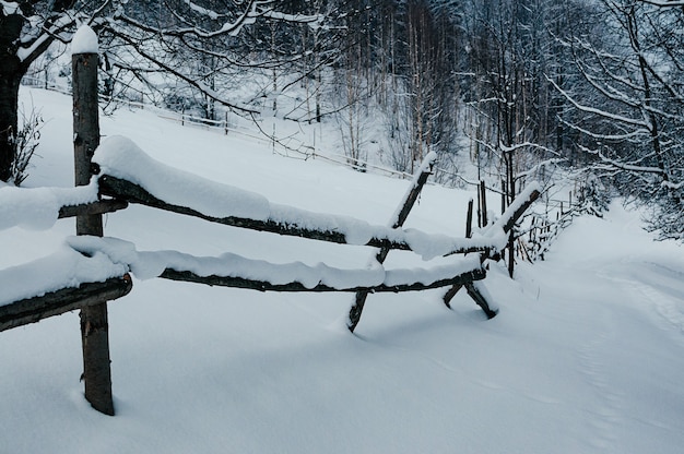 Travi di recinzione in legno ricoperte di berretto da neve paesaggio rurale invernale villaggio o foresta nuvolosa di fattoria