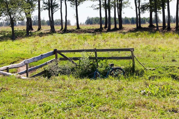 A wooden fence near the bridge over the creek, village landscapes in the summer, near the fence there is a bicycle on which people came to rest