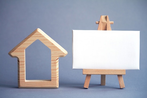 Figura di legno della casa e bordo bianco sul cavalletto in miniatura su gray