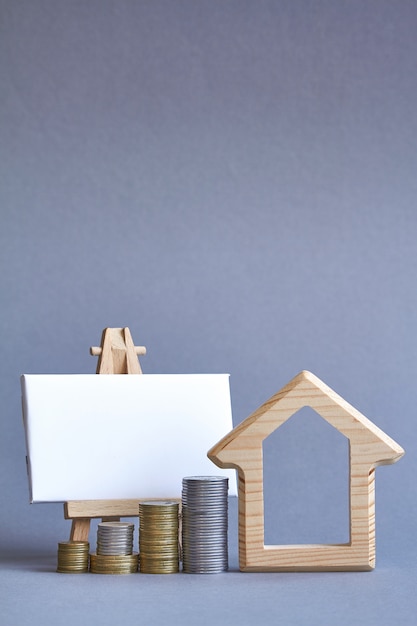 Wooden figure of house with several columns of coins nearby and white board