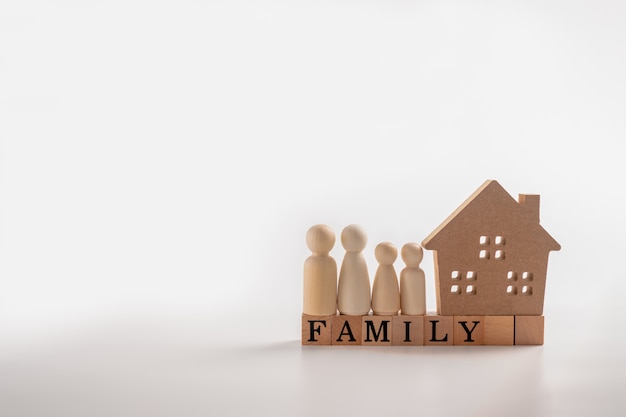 Photo wooden figures family standing beside a wooden house on a wooden cube that writes the word family.