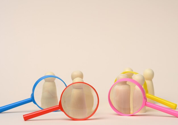 Wooden figures of men stand on a beige background and a plastic magnifying glass. Recruitment concept, search for talented and capable employees, career growth