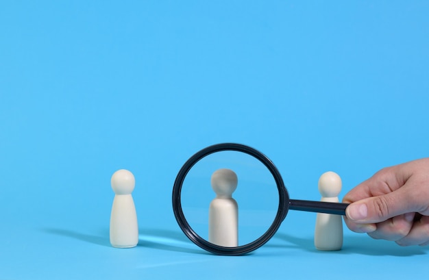 Wooden figures of men stand on a blue surface and a black magnifying glass. Recruitment concept, search for talented and capable employees, career growth