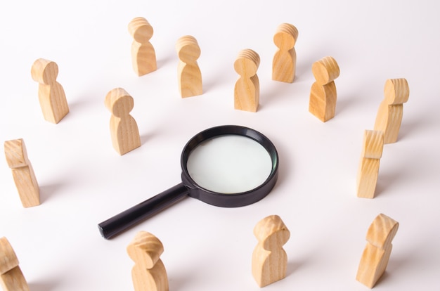 Wooden figures of people stand around the magnifying glass and look to the center.