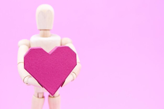 Деревянная статуэтка с бумажной коробкой в форме сердца на розовом фоне