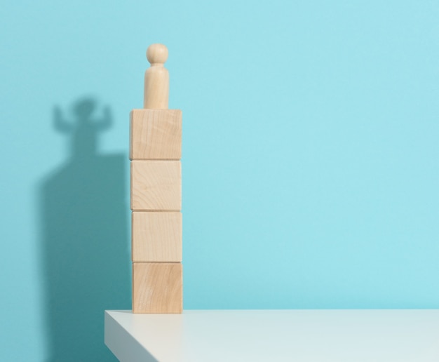 Wooden figurine of a man stands high on the cubes, the shadow of a strong and victorious. Everyone is stronger than he thinks, a superhero. Blue background