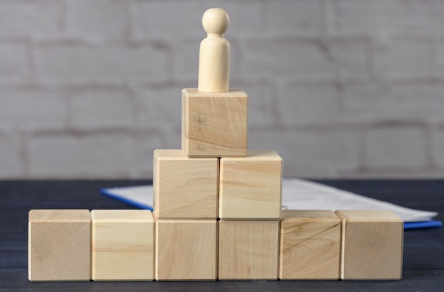 Wooden figurine of a man on top of wooden cubes. The concept of purposefulness, achieving goals, overcoming obstacles