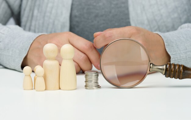 Wooden figurines of a family and magnifier and white coins on the white table. Income growth concept, high percentage of investment. Search for new sources of income, subsidy