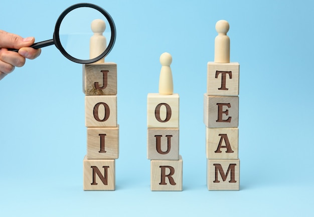 Wooden figurines of men stand on cubes with the inscription and a hand with a magnifying glass on a blue surface