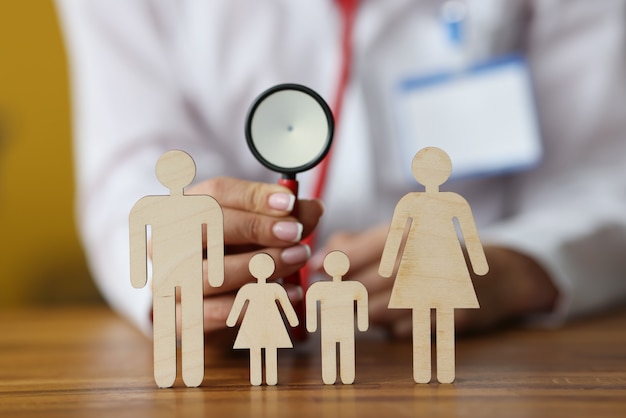 Wooden figurines of parents and children stand on table behind doctor sitting and holding stethoscope