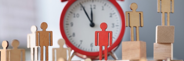 Photo wooden figurines with one red figure stand next to alarm clock