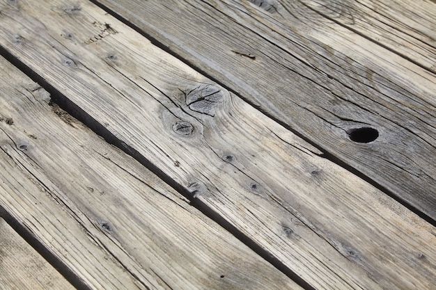 Wooden flooring made of old boards with knots and cracks, weathered by sand. Diagonal view