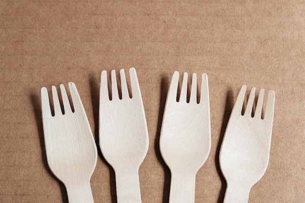 Wooden forks on a cardboard background. Eco friendly disposable tableware. Top view. Copy, empty space for text