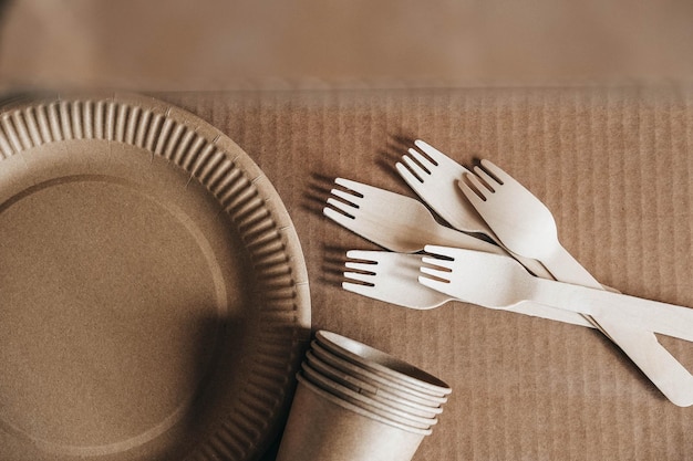 Wooden forks and paper cups with plates on kraft paper background Eco friendly disposable tableware