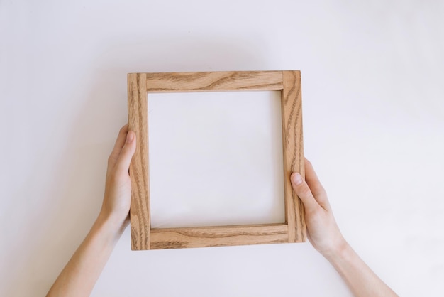 Wooden frame in female hands with place for inscription or photo mockup with a wooden frame on a w