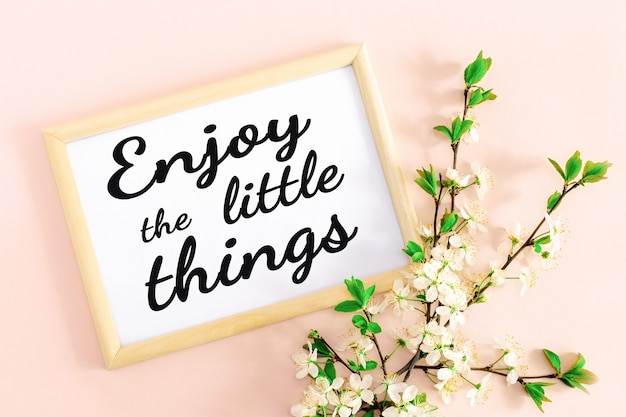 Photo wooden frame with the inscription enjoy the little things, spring inspirational and motivational text and cherry branches with flowers