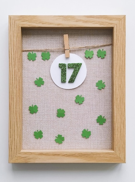 Wooden frame with miniature green numbers 17 with fourleaf clover on fabric background