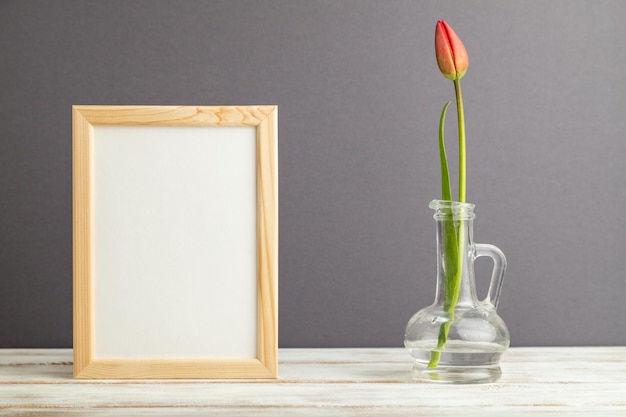 Фото Деревянная рама с красным цветком тюльпана в стекле на сером пастельном фоне, вид сбоку, макет пространства для копирования